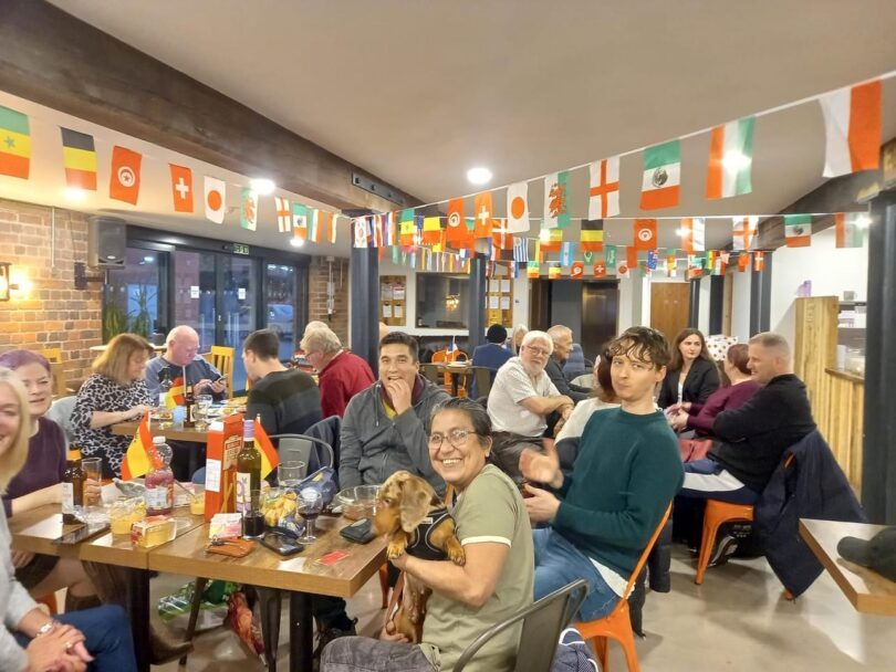 People of different ethnicities sitting at tables in a large room, with the flags of different countries on display