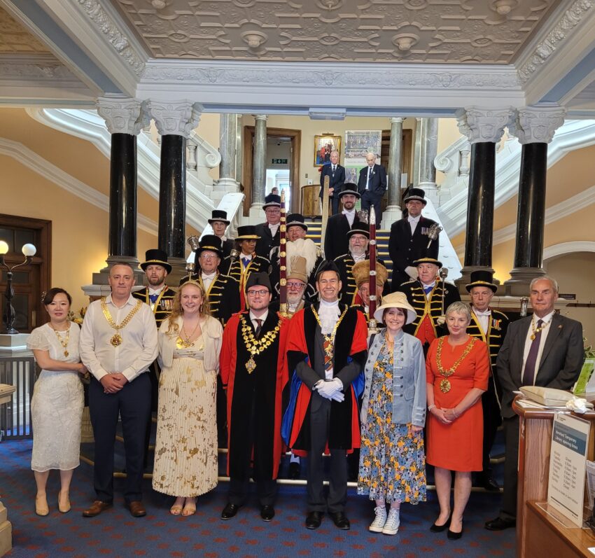 The Mayor and Mayoress  and other dignitaries standing on the steps of an elaborate building with pillars supporting a decorated ceiling