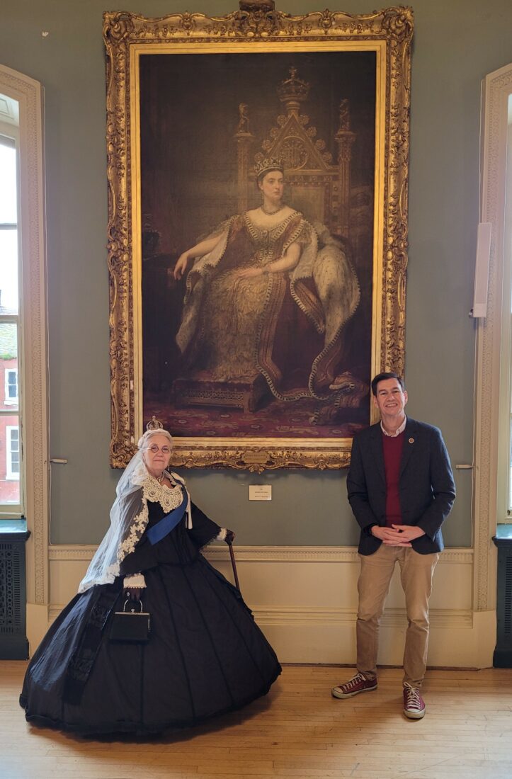 The Mayor and a woman dressed as Queen Victoria standing next to a portrait of the real Queen Victoria in the Guidhall