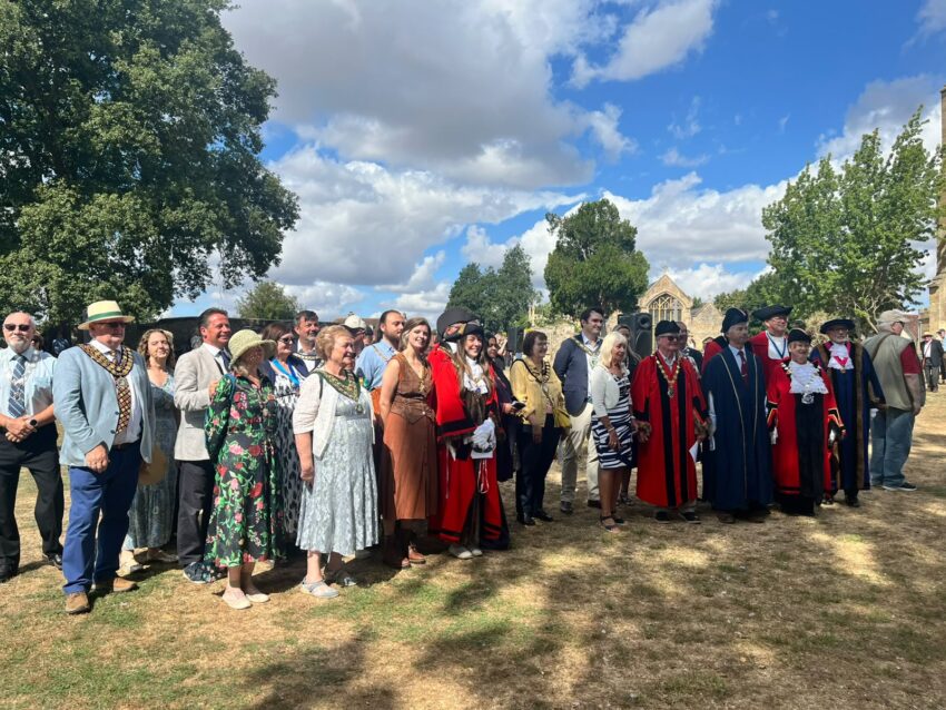 A group of people, several in robes or wearing ceremonial chains, standing in front of Evesham Abbey